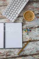 Coffee, pushpin, pencil, computer keyboard and organiser on wooden table