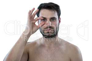 Shirtless man opening his eye with fingers