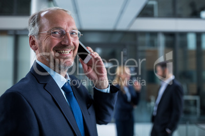 Smiling businessman talking on mobile phone in office corridor