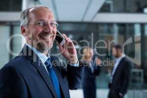 Smiling businessman talking on mobile phone in office corridor