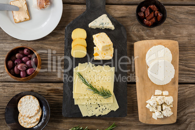Variety of cheese, olives, biscuits and rosemary herbs on wooden table