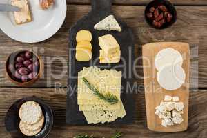 Variety of cheese, olives, biscuits and rosemary herbs on wooden table