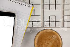 Cup of coffee with keyboard, mobile phone and notepad