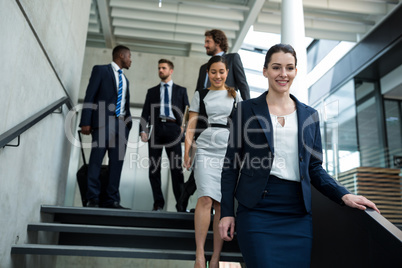 Confident businesswoman with colleagues climbing down the stairs