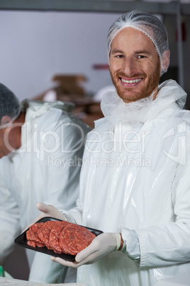 Butcher holding raw meat patties arranged in tray