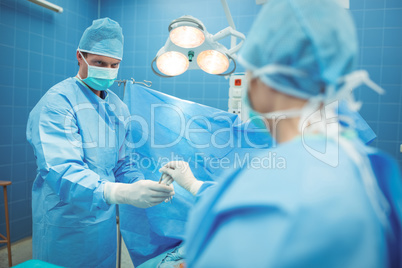 Female surgeon passing surgical tool to her colleague in operation theater