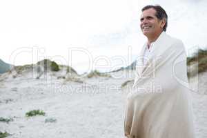 Happy man wrapped in shawl on beach