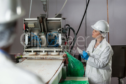 Female technician writing on notepad while examining meat processing machine