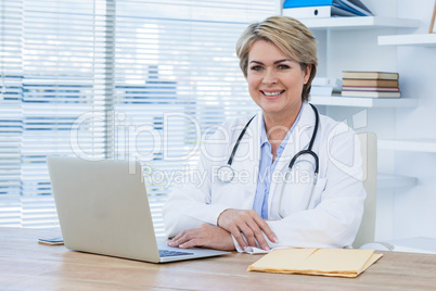 Portrait of smiling female doctor sitting at desk with laptop