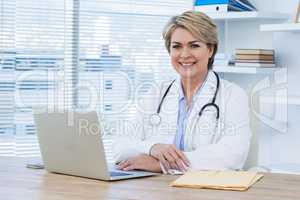 Portrait of smiling female doctor sitting at desk with laptop