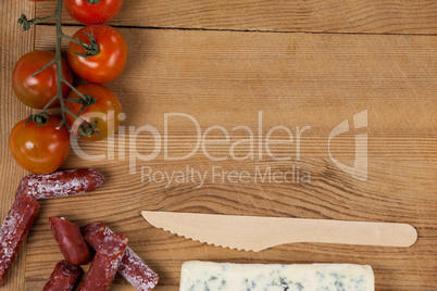 Roquefort cheese, wooden knife, cherry tomatoes and meat on chopping board