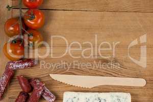 Roquefort cheese, wooden knife, cherry tomatoes and meat on chopping board