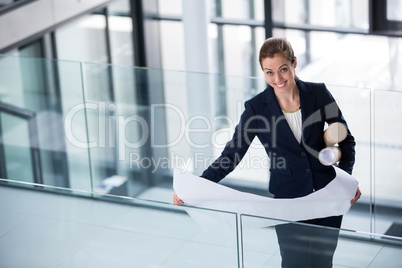 Businesswoman standing at office corridor with blueprint
