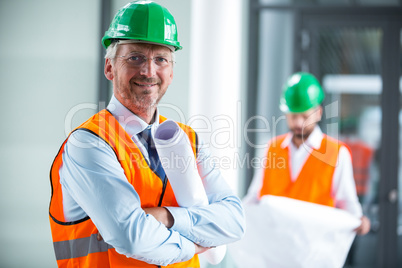 Architect in hard hat standing with blueprint in office corridor