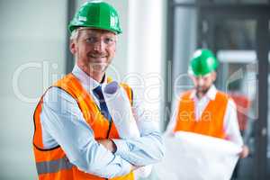 Architect in hard hat standing with blueprint in office corridor