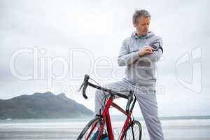 Man with bicycle listening music on mobile phone at beach