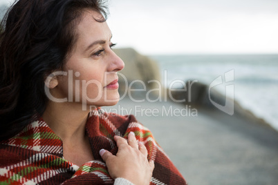 Thoughtful woman wrapped in shawl on beach