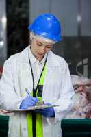 Technician writing on clipboard at meat factory