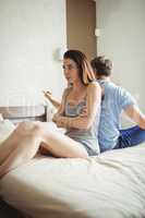 Couple ignoring each other sitting back to back on bed