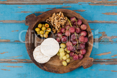 Cheese, grapes, olives and walnuts in wooden bowl