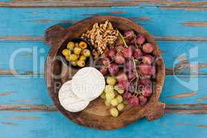 Cheese, grapes, olives and walnuts in wooden bowl