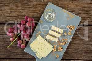 Pieces of cheese, walnut, grapes and glass of wine on tray