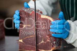 Female butcher cutting raw meat on a band saw machine