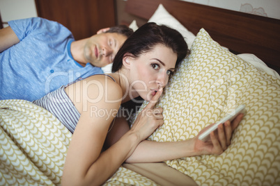 Woman using mobile phone while man sleeping on bed