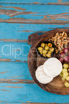 Cheese, grapes, olives and walnuts in wooden bowl