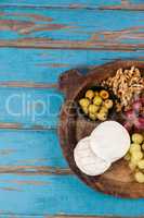 Cheese, grapes, olives and walnuts in wooden bowl