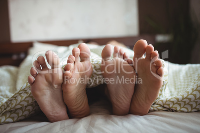 Couple showing their feet while lying on a bed