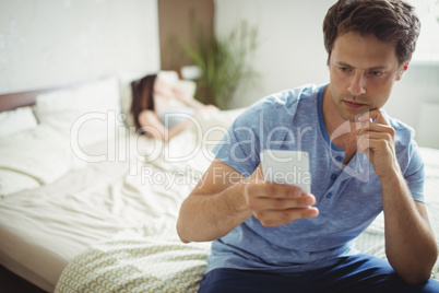 Man using mobile phone while woman sleeping on bed