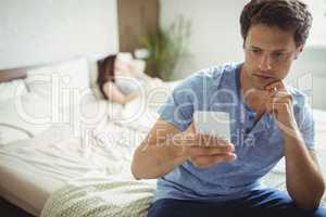 Man using mobile phone while woman sleeping on bed