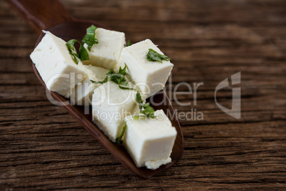 Cheese cubes garnished with herbs on wooden spoon