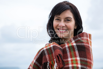 Portrait of happy woman wrapped in shawl on beach