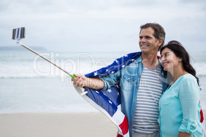 Couple wrapped in american flag taking selfie on beach