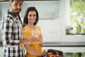 Happy couple toasting glasses of champagne while chopping vegetables in kitchen