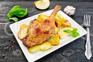 Duck leg with apple and basil in plate on board