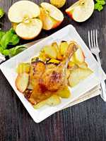 Duck leg with apple and basil in plate on dark board top