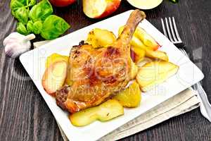 Duck leg with apple and basil in plate on dark board