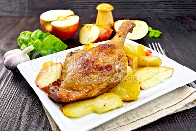Duck leg with apple and potatoes in plate on napkin