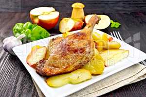 Duck leg with apple and potatoes in plate on napkin