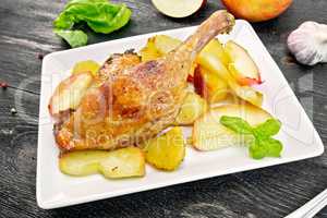 Duck leg with apple and potatoes in plate on board