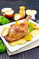 Duck leg with apple and potatoes on dark board
