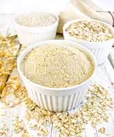 Flour oat in white bowls with bran and flakes on board