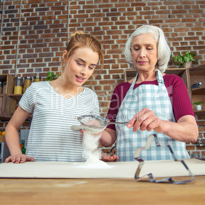 Grandmother and granddaughter sifting flour
