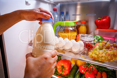 Woman takes the milk from the open refrigerator