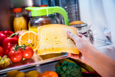 Woman takes the piece of cheese from the open refrigerator