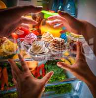 Human hands reaching for sweet cake at night in the open refrige