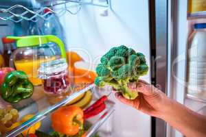 Woman takes the broccoli from the open refrigerator.